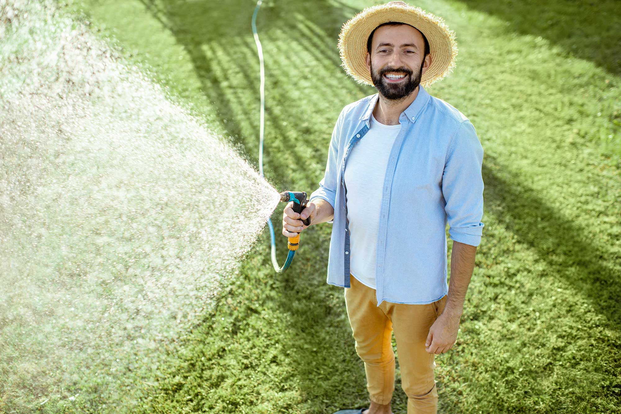 A man smiles at the camera while watering the lawn